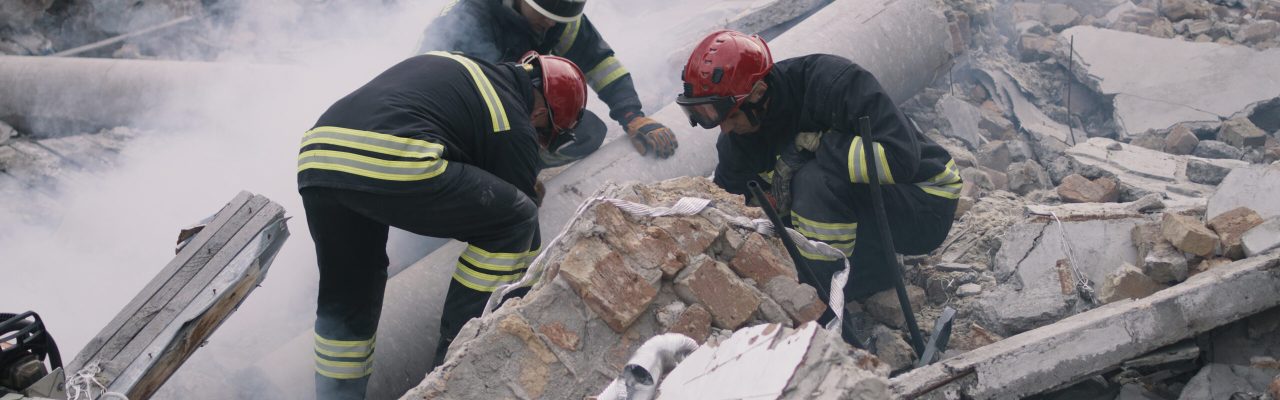 Men in protective uniforms and hardhats removing pieces of broken building during rescue mission after earthquake