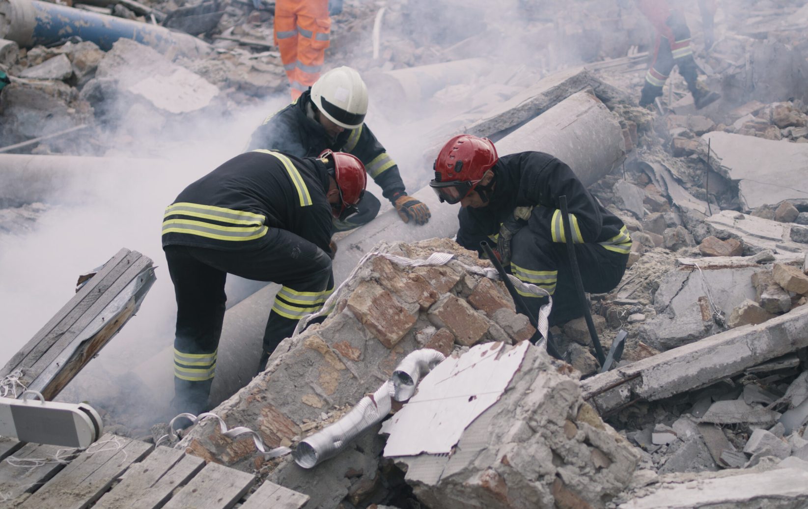 Men in protective uniforms and hardhats removing pieces of broken building during rescue mission after earthquake