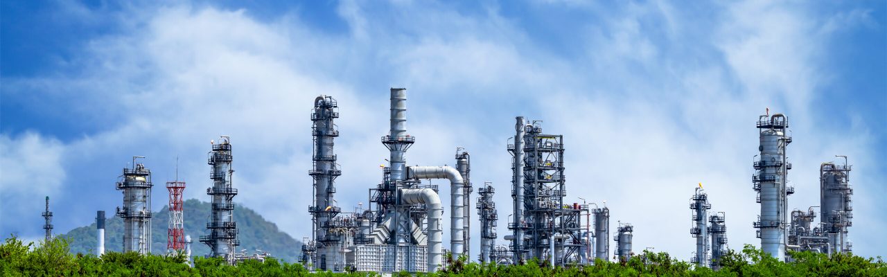 Oil refinery plant from industry zone, Oil and gas petrochemical industrial with tree and blue sky background, Refinery factory oil storage tank and pipeline steel, Ecosystem and healthy environment concepts.